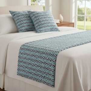 May include: A bed with white sheets, a bed skirt, and two pillows. The pillows and bed runner feature a geometric pattern in shades of teal, gray, and white. The bed runner is placed at the foot of the bed.