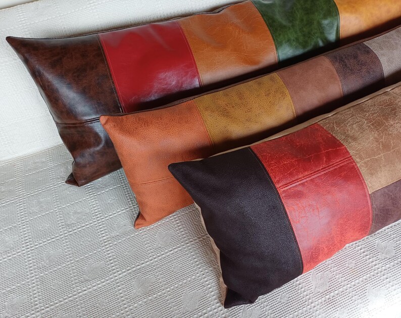 May include: Three rectangular throw cushions featuring a colour-blocked design with panels of faux leather in shades of dark brown, red, orange, yellow, green, and tan. Each cushion has a textured surface and is arranged in a staggered, overlapping row.