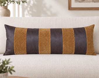 May include: A rectangular lumbar pillow featuring alternating vertical stripes of dark brown faux leather and textured mustard yellow fabric. The pillow has a long, horizontal orientation with a clean, stitched finish along the edges.