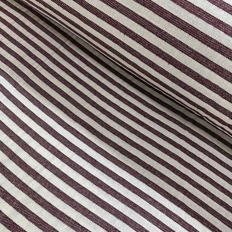 May include: White and burgundy striped fabric with a subtle texture. The fabric is woven with thin stripes of burgundy against a white background.
