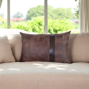 May include: A brown leather cushion with a dark brown leather strip down the centre. The cushion is on a light beige sofa.