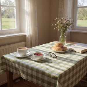 May include: A table set for breakfast with a green and white checkered tablecloth. A cup of coffee, a bowl of berries, and a plate of rolls are on the table. A vase of flowers and a book are also present.