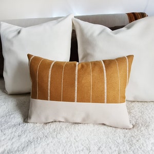 May include: Two white throw pillows and a decorative pillow with a mustard yellow and white striped pattern. The striped pillow has a white bottom section.