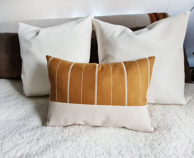 May include: Two white throw pillows and a decorative pillow with a mustard yellow and white striped pattern. The striped pillow has a white bottom section.