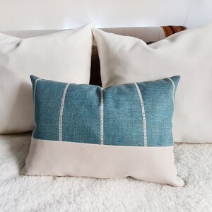 May include: Two white throw pillows with a blue and white striped pillow in front of them. The pillows are on a white fluffy bedspread.