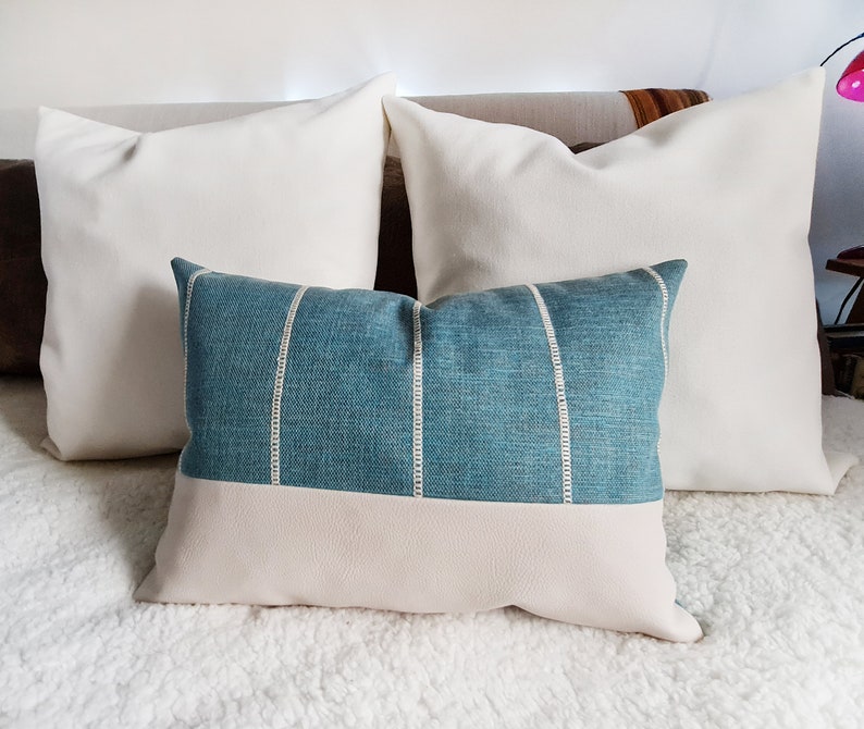 May include: Two white throw pillows with a blue and white striped pillow in front of them. The pillows are on a white fluffy bedspread.