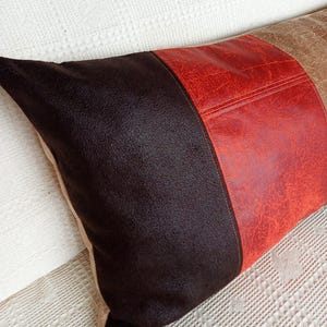 May include: A rectangular throw pillow featuring three distinct vertical panels of textured material. The left section is dark brown, the centre panel is a vibrant red, and the right section is a light tan, all with a visible grain.