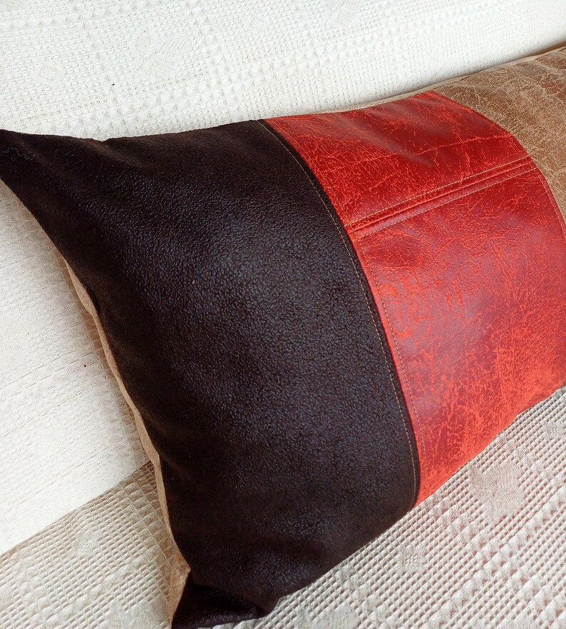 May include: A rectangular throw pillow featuring three distinct vertical panels of textured material. The left section is dark brown, the centre panel is a vibrant red, and the right section is a light tan, all with a visible grain.