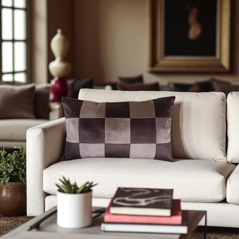 May include: A rectangular decorative pillow with a checkerboard pattern in shades of brown and gray. The pillow is placed on a cream-colored sofa in a living room setting. Other pillows and decor are visible in the background.