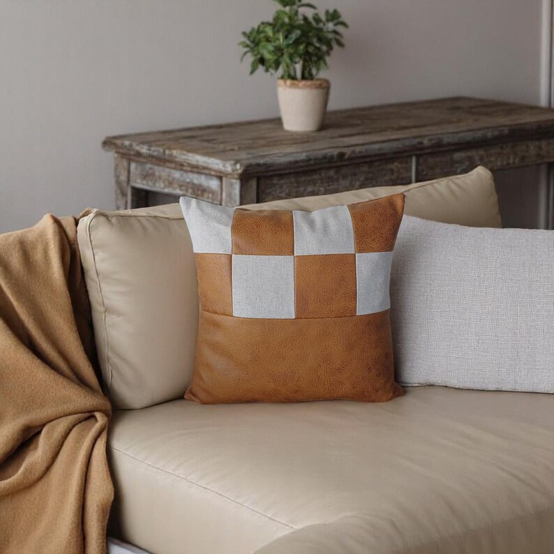 May include: A light brown and white checkered throw pillow with a faux leather front and a light brown throw blanket on a beige couch.