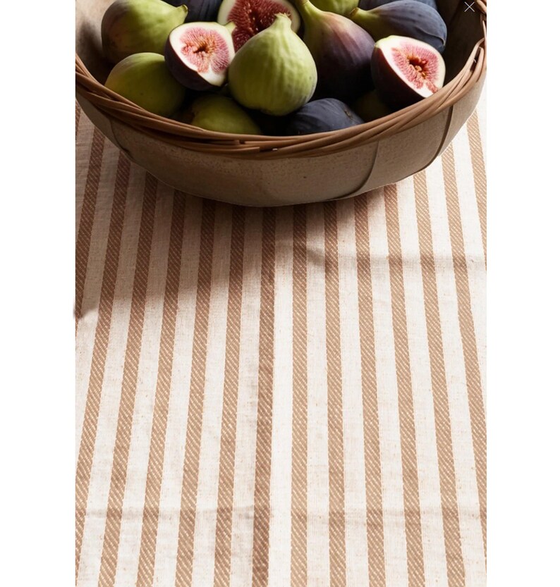 May include: A brown and white striped tablecloth with a bowl of fresh figs in the center.