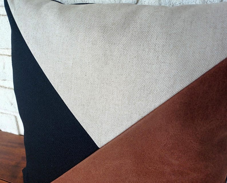 May include: A decorative pillow with a geometric design. The pillow features a black, beige, and brown color scheme. The pillow is made of a textured fabric and has a modern aesthetic.