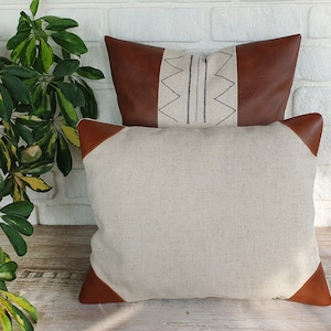 May include: Two throw pillows, one with a brown leather exterior and a geometric pattern, and the other with a beige linen exterior.