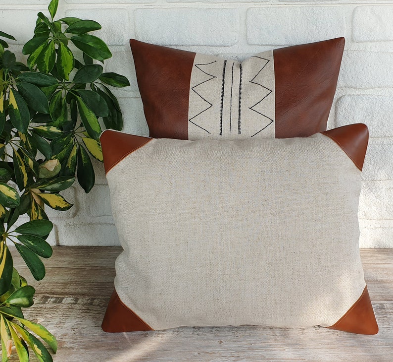 May include: Two throw pillows, one with a brown leather exterior and a geometric pattern, and the other with a beige linen exterior.