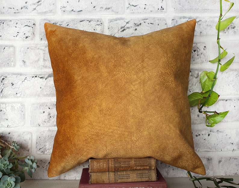 May include: A brown leather pillow with a textured surface. The pillow is sitting on a stack of books.
