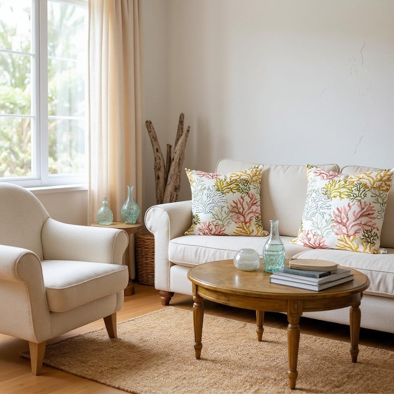 Pu&ograve; includere: Soggiorno con divano e poltrona color crema. Cuscini decorativi con motivi di barriera corallina adornano il divano. Un tavolino rotondo in legno poggia su un tappeto di iuta. Vasi di vetro e legno galleggiante completano il tema costiero.