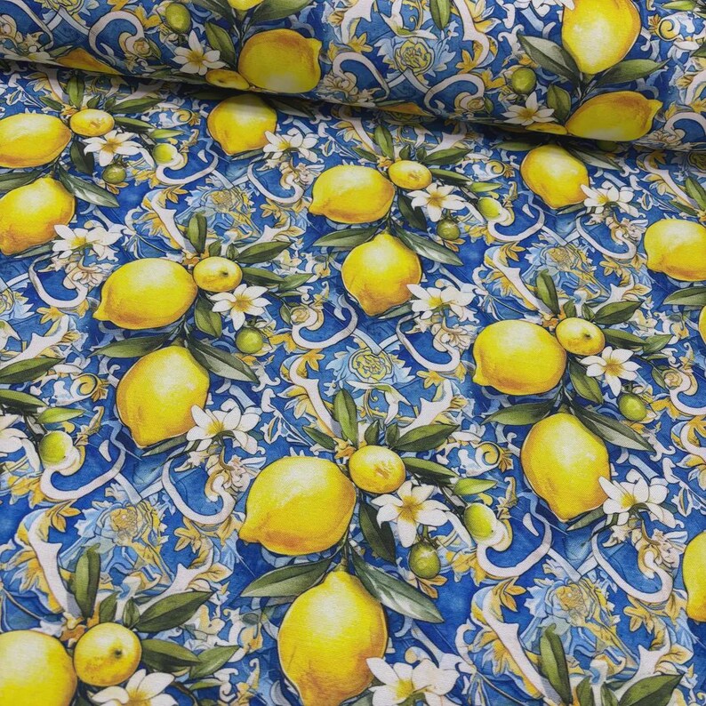 May include: A fabric with a repeating pattern of yellow lemons, white flowers, and green leaves on a blue background. The design has a vintage, botanical feel, with a scroll-like pattern in the background.