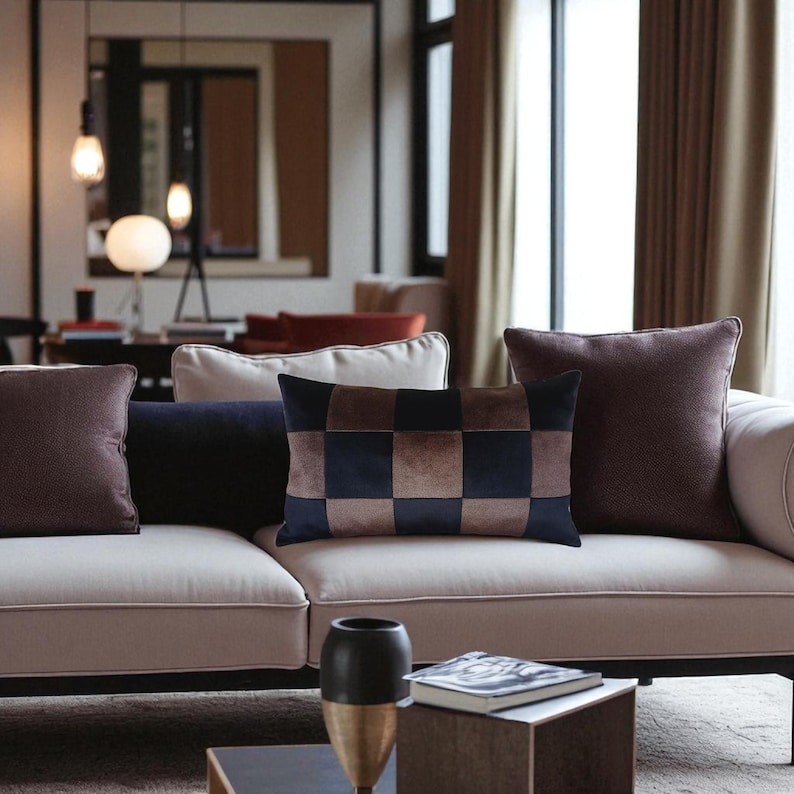 Puede incluir: Un sof&aacute; color crema est&aacute; adornado con varias almohadas decorativas de varias formas y colores. Las almohadas incluyen patrones lisos burdeos, azul marino y a cuadros en marr&oacute;n y azul marino. Un ambiente de sala de estar moderno con mesa de centro y jarr&oacute;n decorativo.