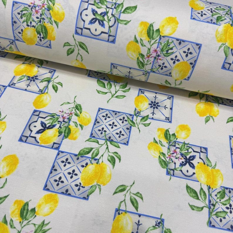 May include: White fabric with a repeating pattern of yellow lemons, green leaves, and blue and white tile-like squares. The design has a fresh, summery feel, perfect for home decor or apparel.