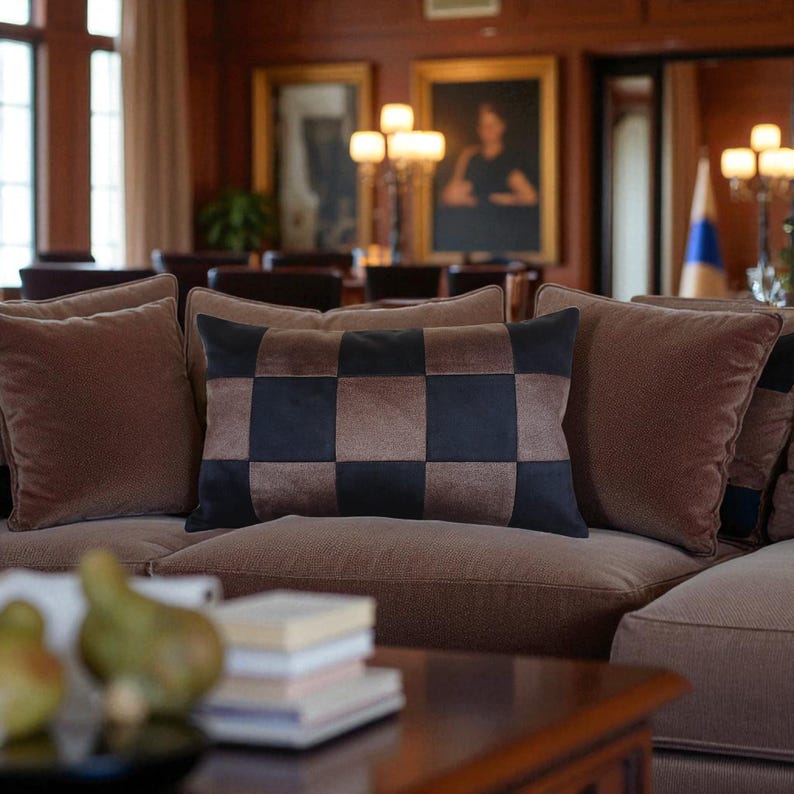 Puede incluir: Un sof&aacute; marr&oacute;n con varias almohadas. La almohada central tiene un patr&oacute;n de tablero de ajedrez en negro y marr&oacute;n. Otras almohadas son de color marr&oacute;n liso. El sof&aacute; est&aacute; en una habitaci&oacute;n con pinturas y l&aacute;mparas.