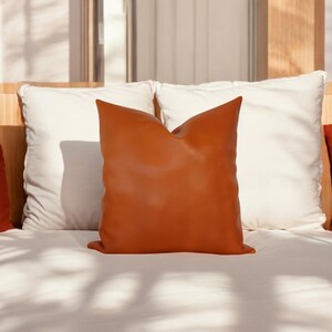 May include: A burnt orange leather pillow on a white bed with white pillows.