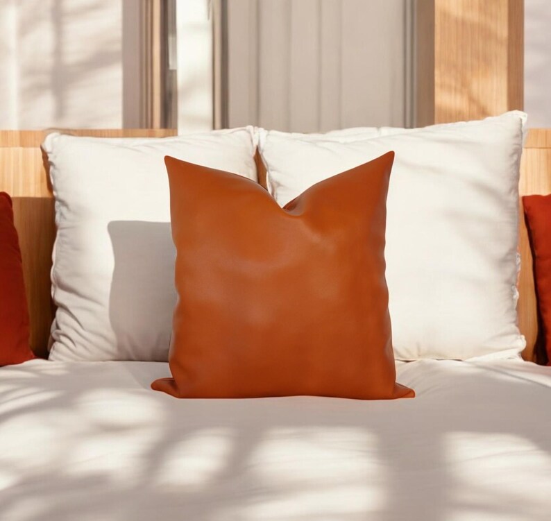 May include: A burnt orange leather pillow on a white bed with white pillows.