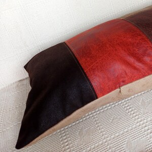 May include: A rectangular throw pillow featuring a colour-blocked design with a dark brown suede-like panel on the left, a vibrant red textured centre panel, and a light tan panel on the right side, finished with visible stitching.