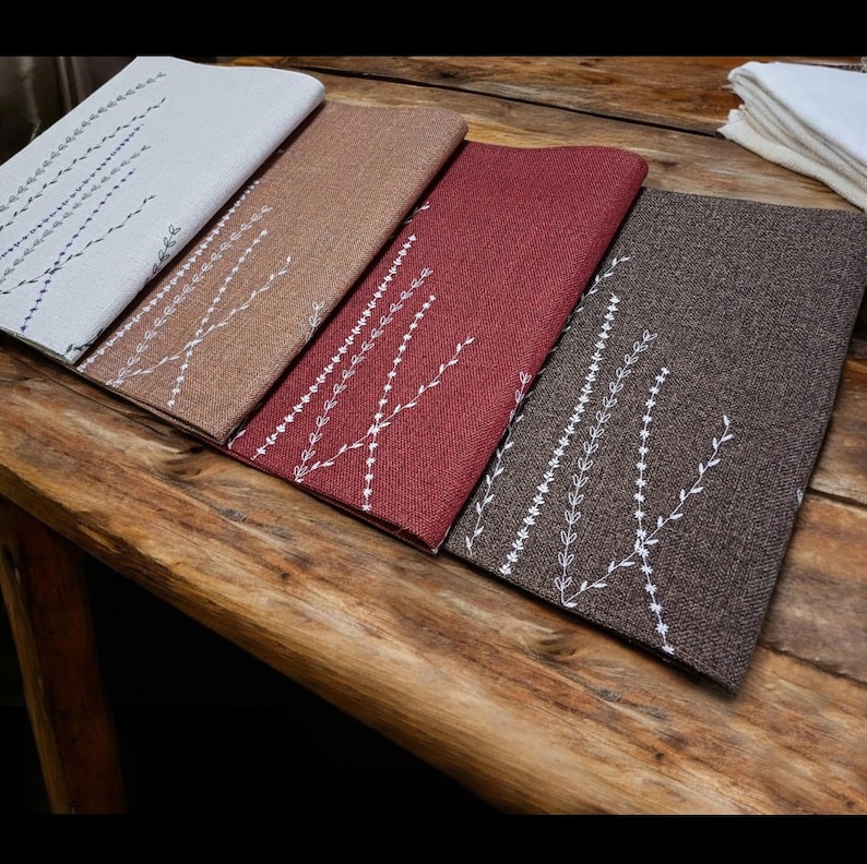 May include: Four placemats with a white floral design on a brown wooden table. The placemats are in different colors: white, brown, red, and gray.