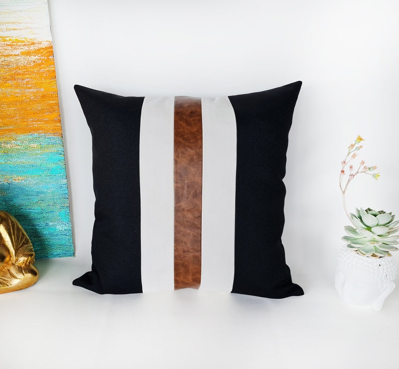 May include: Black and white striped cushion with a brown leather accent strip. The cushion is made of a soft, comfortable fabric and has a simple, modern design.