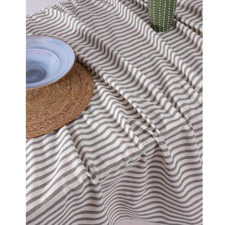 May include: A white and gray striped tablecloth with a woven texture. The tablecloth is made of cotton and is perfect for a casual dining setting.