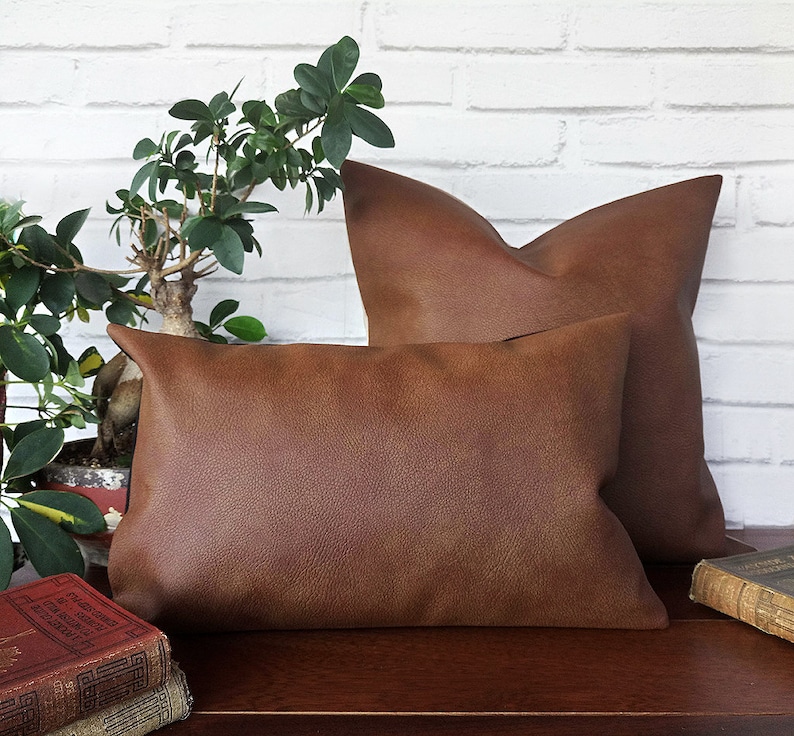 May include: Two brown leather throw pillows on a wooden surface with a potted plant in the background.