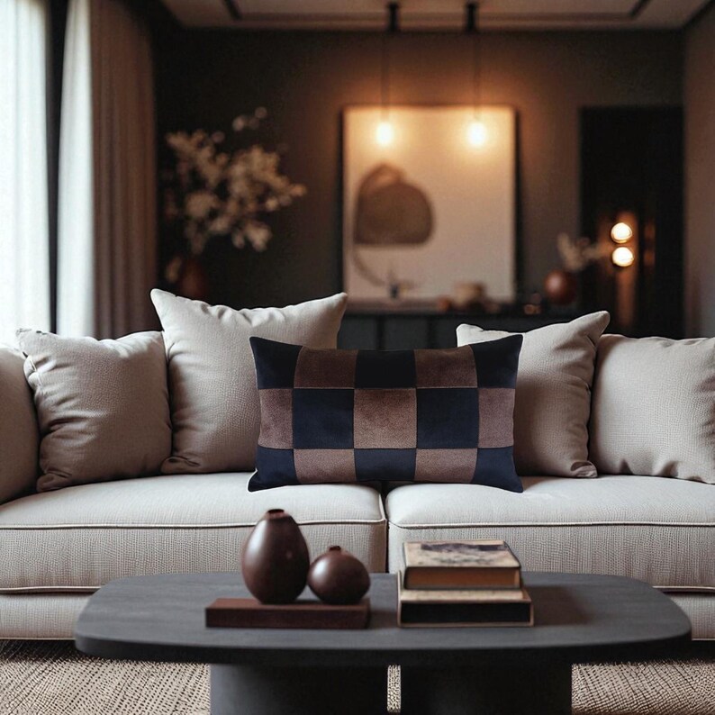 Puede incluir: Un coj&iacute;n rectangular decorativo con un patr&oacute;n a cuadros en tonos marr&oacute;n y azul marino descansa sobre un sof&aacute; color crema. El coj&iacute;n es el punto focal de un ambiente acogedor de sala de estar, con almohadas de tonos neutros y una mesa de centro oscura.