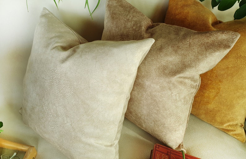 May include: Three decorative throw pillows in various shades of brown. The pillows are made of a soft, textured fabric.