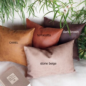May include: Four decorative throw pillows in various colors and textures. The pillows are arranged in a row on a white surface. The colors are camel, terracotta, stone beige, and dark brown.