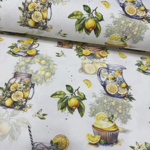 May include: White fabric with a repeating pattern of lemons, lemon slices, and floral arrangements. The design includes images of a teacup, a cupcake, and a pitcher filled with lemonade. The lemons are yellow with green leaves.