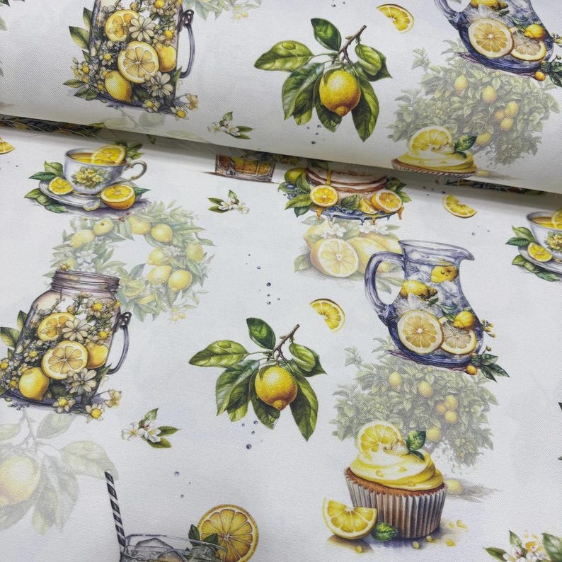 May include: White fabric with a repeating pattern of lemons, lemon slices, and floral arrangements. The design includes images of a teacup, a cupcake, and a pitcher filled with lemonade. The lemons are yellow with green leaves.