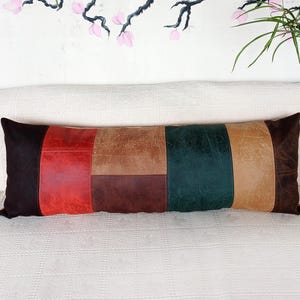 May include: A rectangular lumbar cushion featuring a patchwork design of leather-effect panels in dark brown, vibrant red, tan, deep chocolate brown, and forest green. The cushion has a smooth, multi-textured surface with visible stitching.