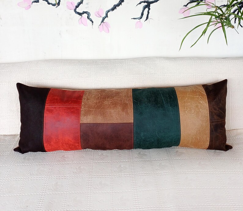 May include: A rectangular lumbar cushion featuring a patchwork design of leather-effect panels in dark brown, vibrant red, tan, deep chocolate brown, and forest green. The cushion has a smooth, multi-textured surface with visible stitching.