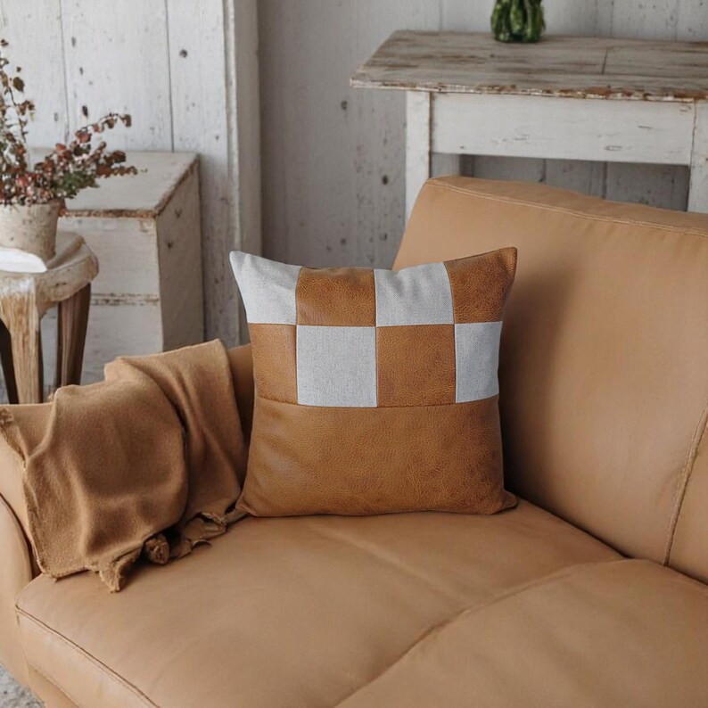 May include: A brown leather sofa with a throw blanket and a brown and white checkered throw pillow. The pillow has a brown leather front and a white fabric back.
