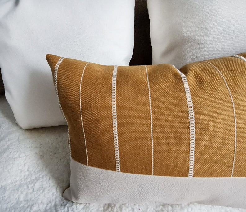May include: A mustard yellow throw pillow with white piping and a white stripe pattern. The pillow has a white bottom edge.