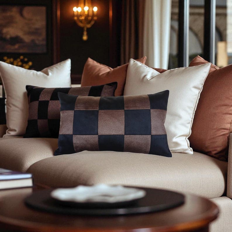 Puede incluir: Un sof&aacute; con varias almohadas decorativas. Las almohadas incluyen un patr&oacute;n a cuadros en marr&oacute;n y negro, almohadas blancas lisas y de color &oacute;xido. El sof&aacute; es de color beige neutro.