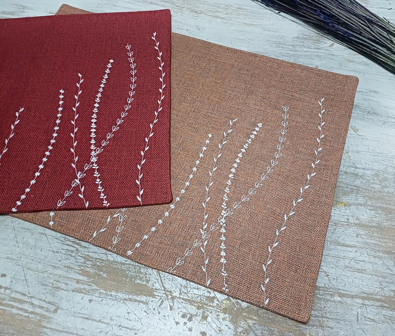 May include: Two placemats with a white embroidered design of stylized leaves on a red and brown background.