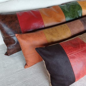 May include: Three rectangular throw pillows made of faux leather with a textured finish. Each pillow features a colour-blocked design with panels in shades of dark brown, red, orange, yellow, green, and tan, arranged in horizontal stripes.