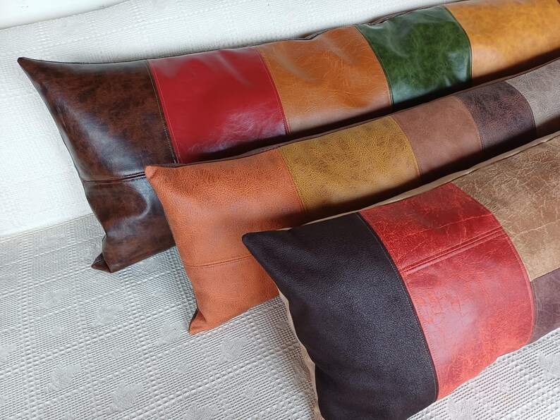May include: Three rectangular throw pillows made of faux leather with a textured finish. Each pillow features a colour-blocked design with panels in shades of dark brown, red, orange, yellow, green, and tan, arranged in horizontal stripes.