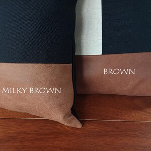 May include: Two decorative throw pillows with a color block design. The top portion of each pillow is navy blue, with a white stripe on one. The bottom section is a brown suede-like material. One pillow has the text "Milky Brown" and the other has "Brown".