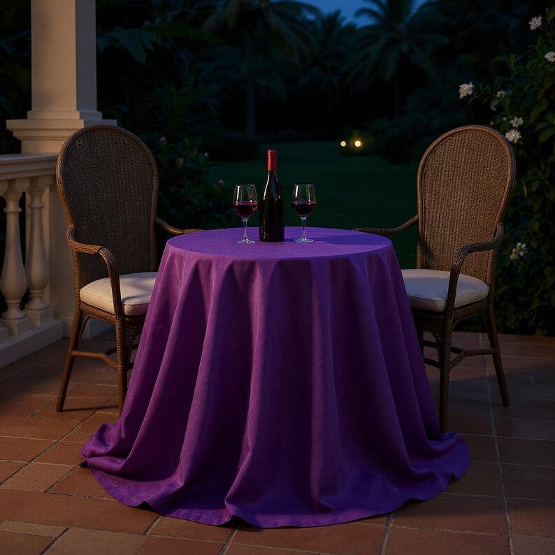 May include: A round table covered with a vibrant purple tablecloth, set for a romantic evening. Two wicker chairs flank the table, with a bottle of wine and two glasses. The scene is set outdoors at dusk.