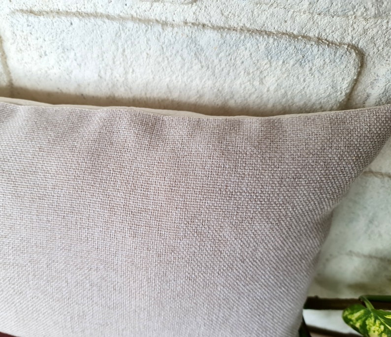 May include: A close-up of a light beige pillow with a white border. The pillow is made of a soft, textured fabric.