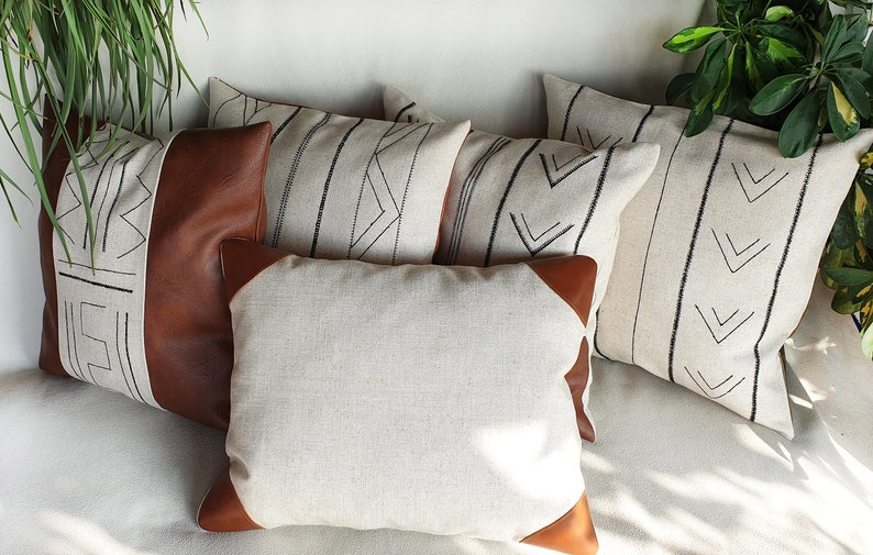 May include: Five decorative throw pillows with geometric patterns. The pillows are made of a light beige linen fabric with black embroidery. Two of the pillows have brown leather accents.