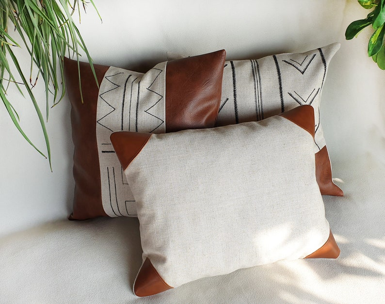 May include: Three decorative throw pillows with geometric patterns. The pillows are made of a beige linen fabric with brown leather accents. The patterns are black and white.