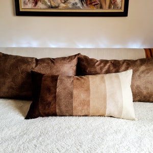 May include: A set of four throw pillows with a brown, beige and white striped pattern. The pillows are arranged on a white bedspread.